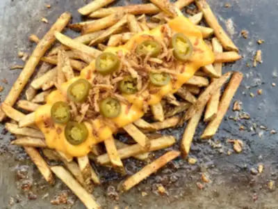 Concept imagery: golden hand-cut fries with cheese sauce, pickled jalapeno and crispy onion on the griddle